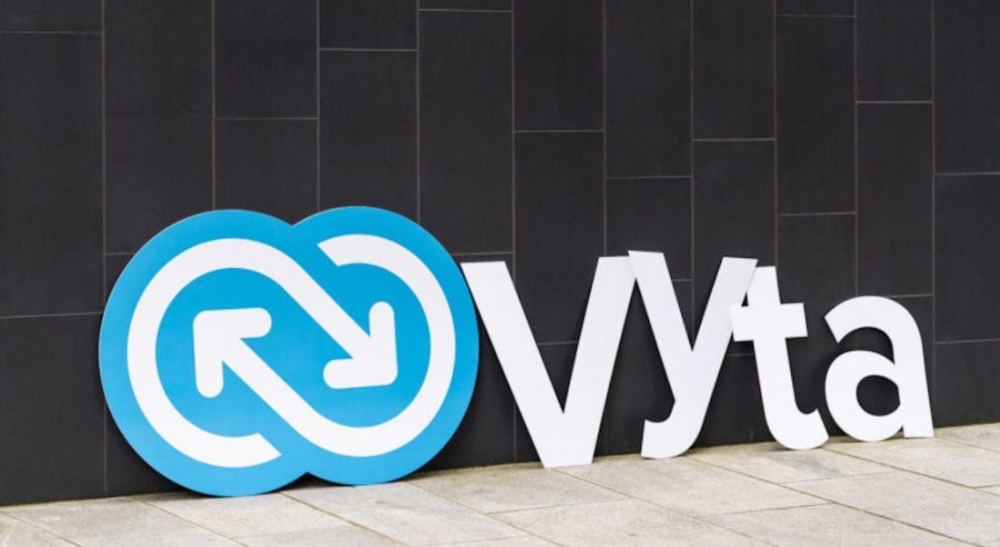 A large cut-out of the new Vyta logo propped up against a grey stone wall.