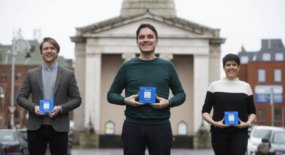 The three co-founders of FoodMarble stand outdoors, each holding a box containing the Aire device.