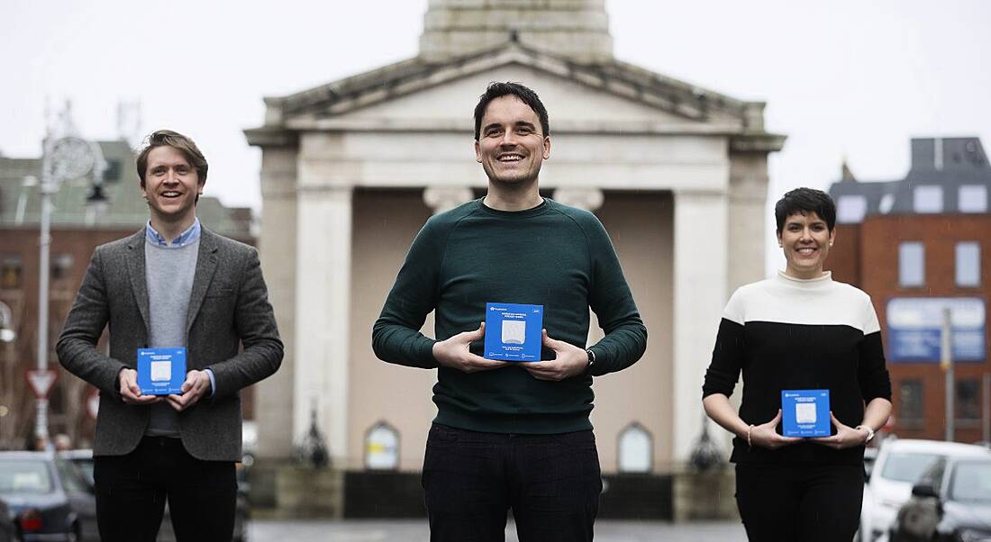 The three co-founders of FoodMarble stand outdoors, each holding a box containing the Aire device.