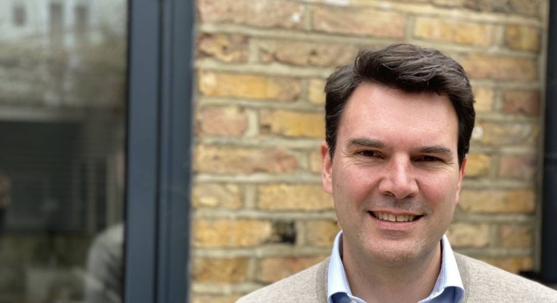 Constantin Beier of Aon is standing outside in front of a brick wall smiling into the camera.