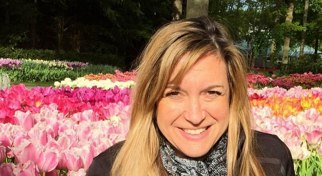 Stacey Wasserman is outdoors in front of colourful flowers in a park.