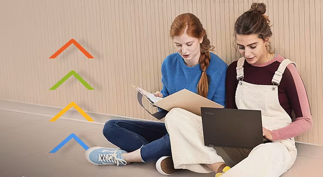 Two teenage girls sitting cross-legged on a floor with laptops as if they are students.