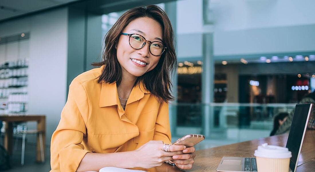 Remote working woman working at a desk on a laptop drinking a coffee and smiling.