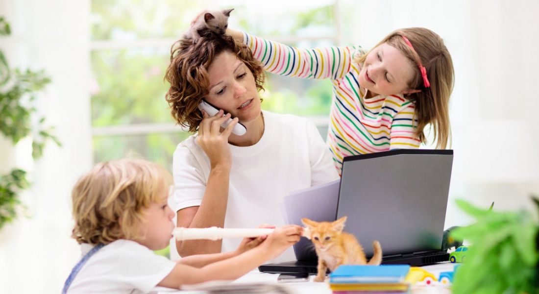 Woman trying to work from home being bothered by two small kids and their kittens. One child is putting a kitten in her hair.
