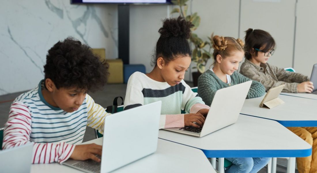 Four young school children sitting at a row of desks working on computers.