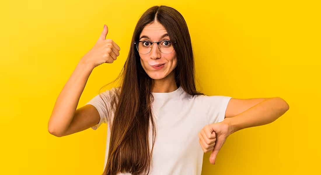 Woman doing thumbs up with one hand and thumbs down with the other as though evaluating a remote job. She is standing against a yellow background.