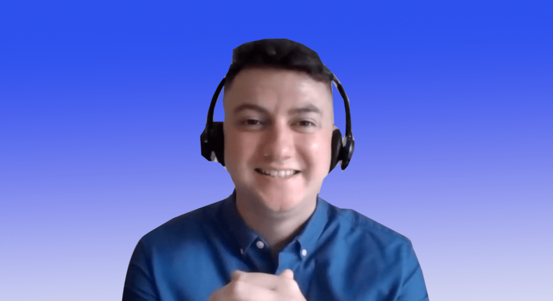 A young man in a blue shirt wearing a headset smiles at the camera against a blue background that fades down to white.