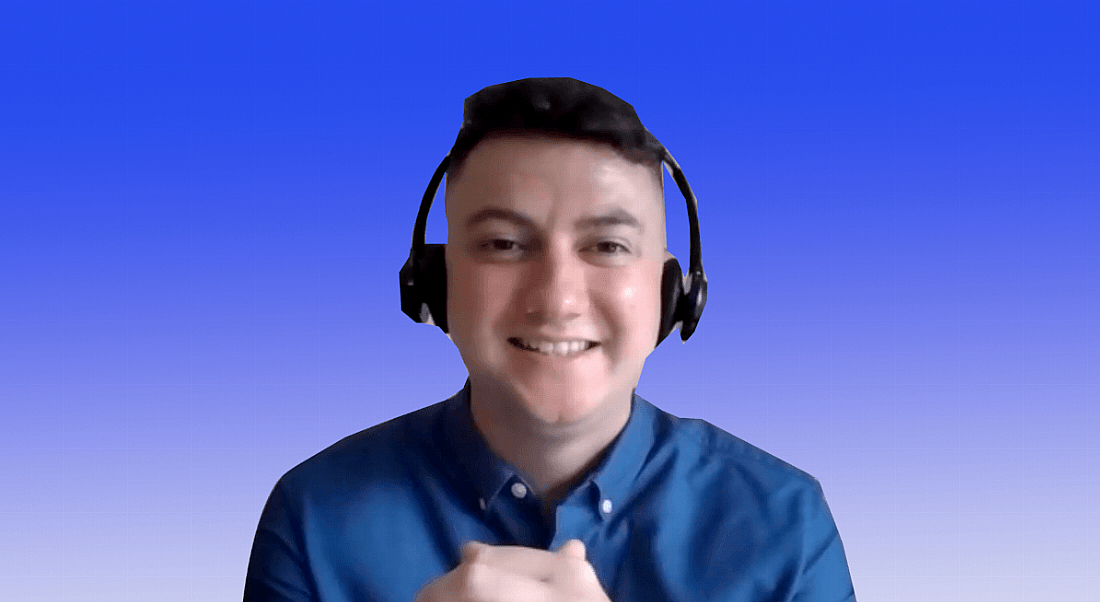 A young man in a blue shirt wearing a headset smiles at the camera against a blue background that fades down to white.