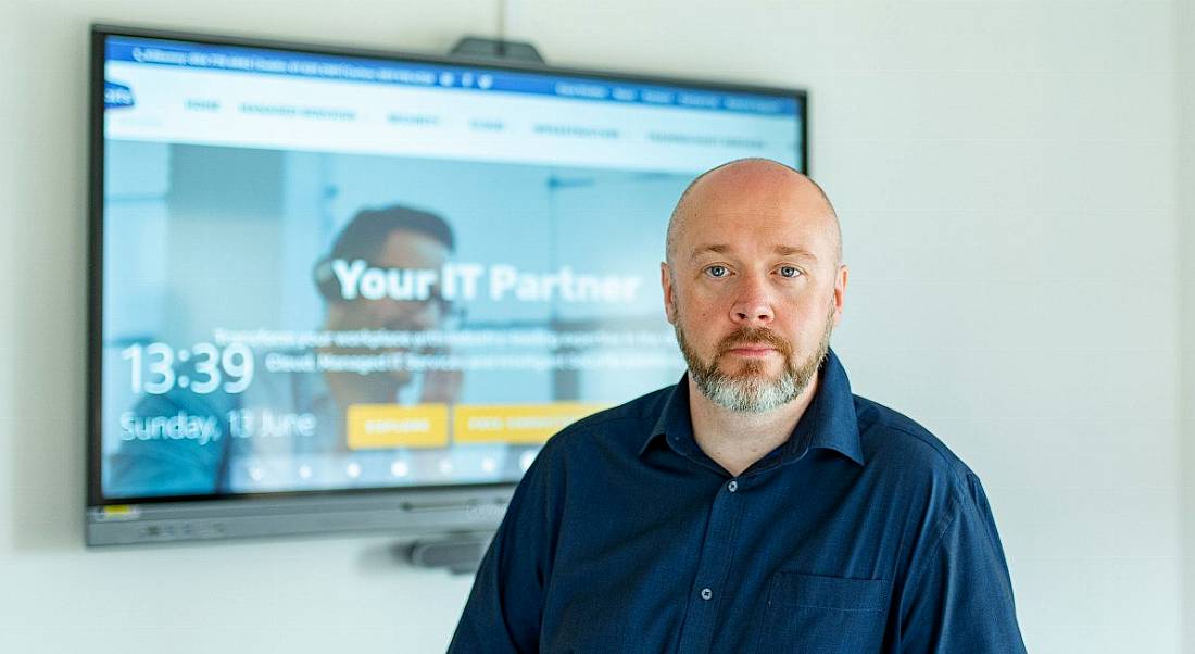 Gavin Dixon, CEO of BITS, standing in a room with a TV monitor behind him with BITS' website displayed on it.