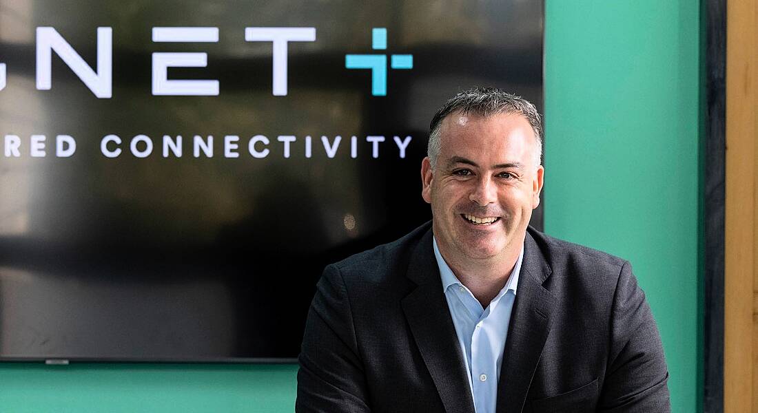 A man in a suit smiling at the camera. Behind him is a wall that shows the second half of the Magnet Plus logo.