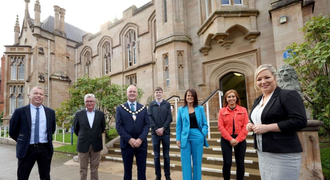 Northern Ireland Deputy First Minister Michelle O'Neill with students and industry stakeholders standing outside a stone building at Ulster University's Magee campus.