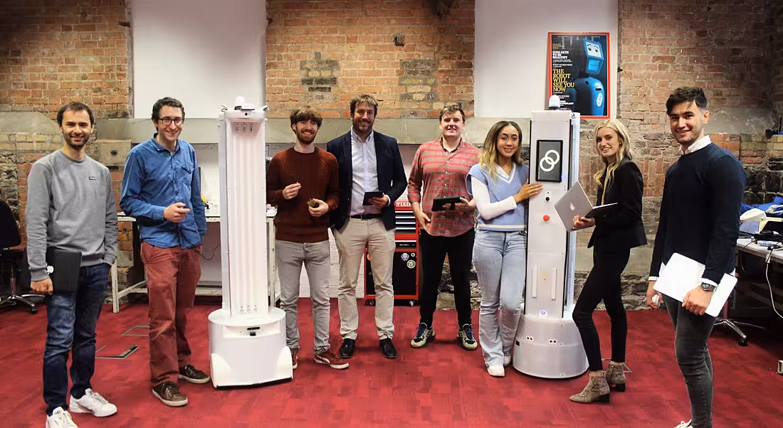 A group of people stand around two tall, white robots.
