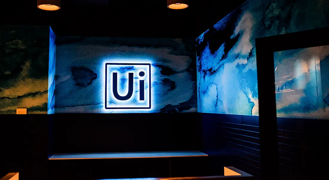 UiPath logo lit up by blue lights on a blue wall.