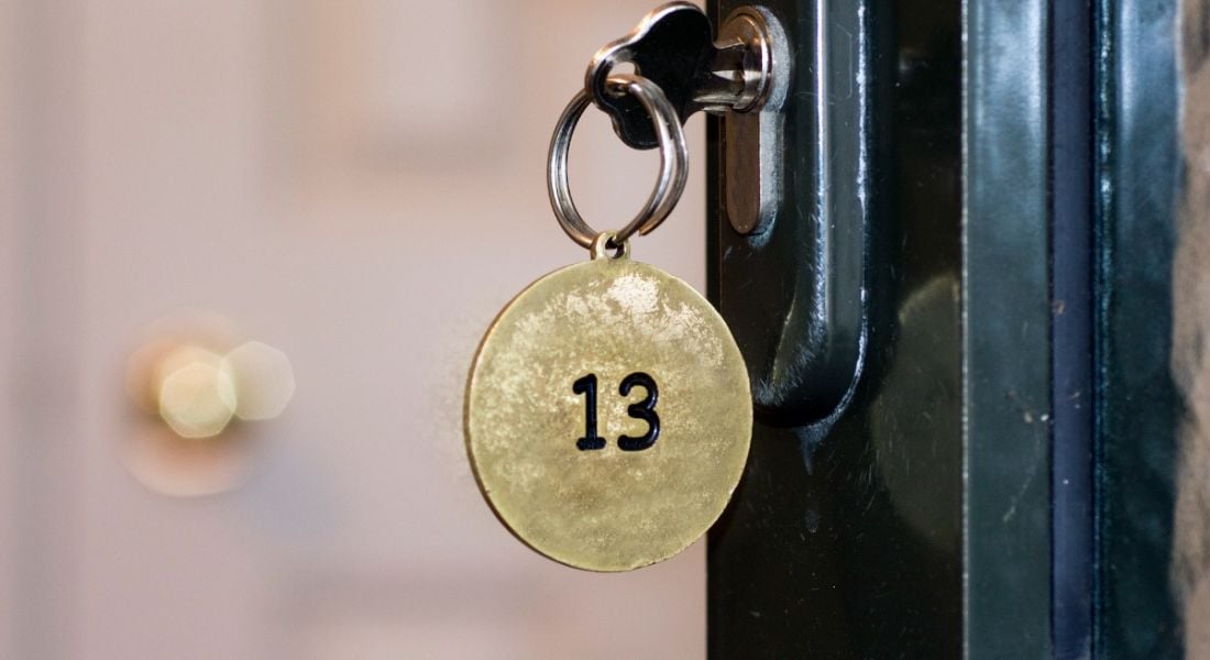 A gold round keyring with the number 13 on it. It’s attached to a key in a black door.