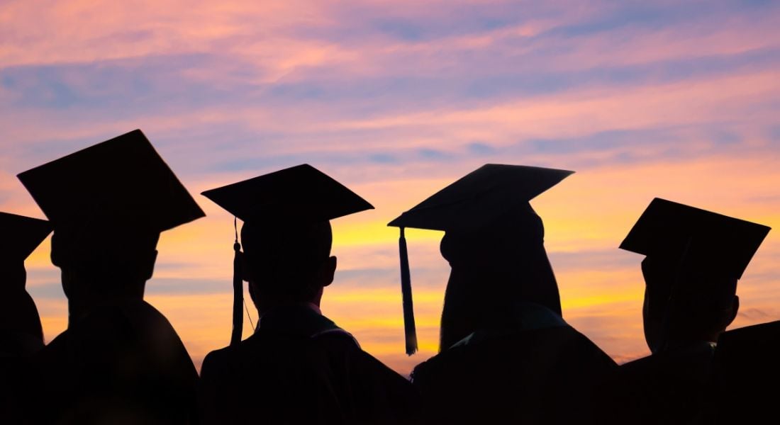 A silhouette of several graduates staring at a colourful sky at sunset.