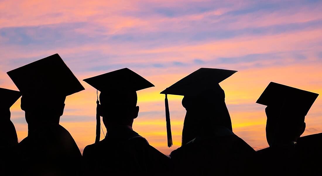 A silhouette of several graduates staring at a colourful sky at sunset.