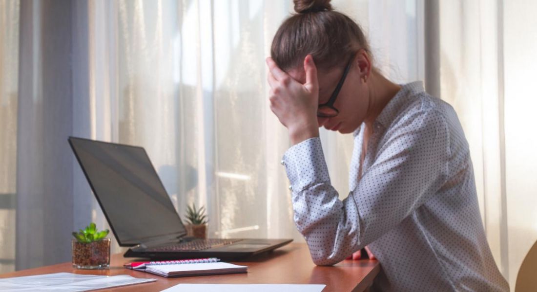 A woman with her head in her hand, showing her frustration while sitting at a laptop working remotely.