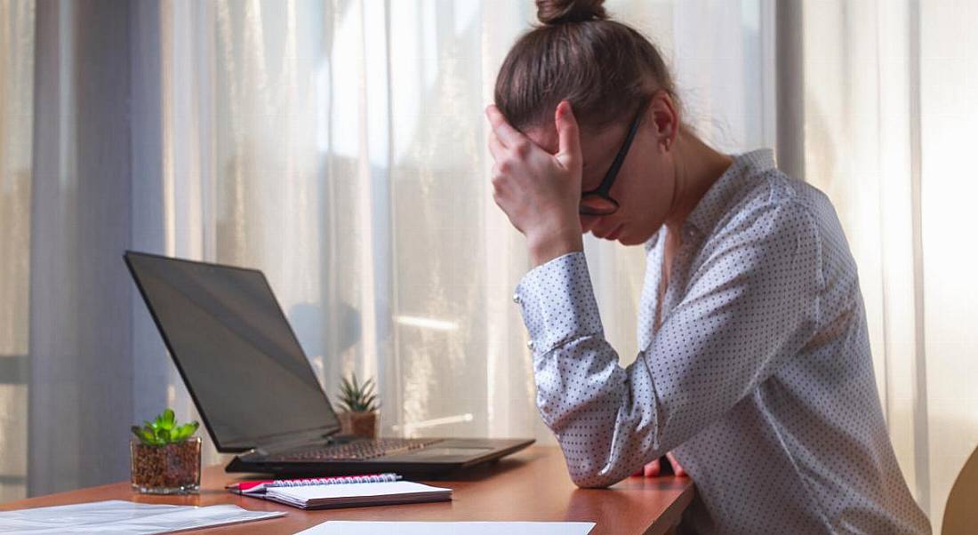 A woman with her head in her hand, showing her frustration while sitting at a laptop working remotely.