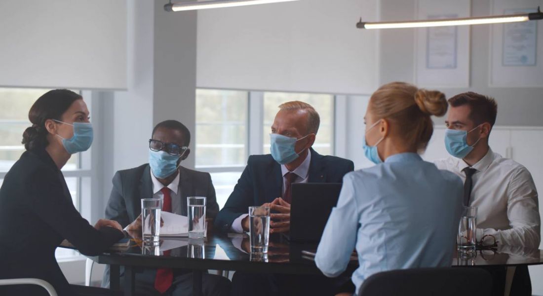 A group of businesspeople sit around a table in an office, all wearing face masks.