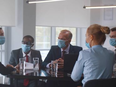 A group of businesspeople sit around a table in an office, all wearing face masks.