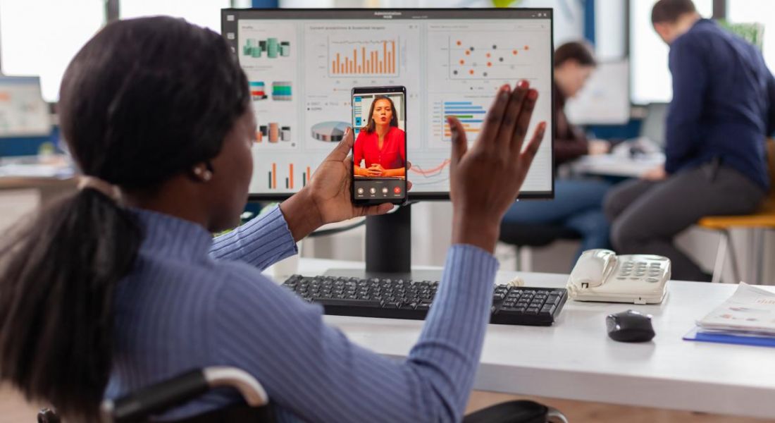 A young woman in a wheelchair is remote working, having a virtual conversation via her smartphone.