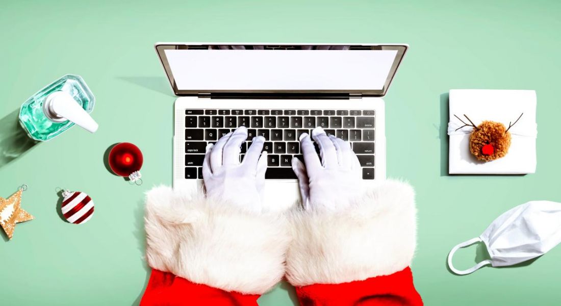 Christmas gift giving: Santa Claus using a laptop shot from above with hand sanitiser and a mask and festive decorations beside him.