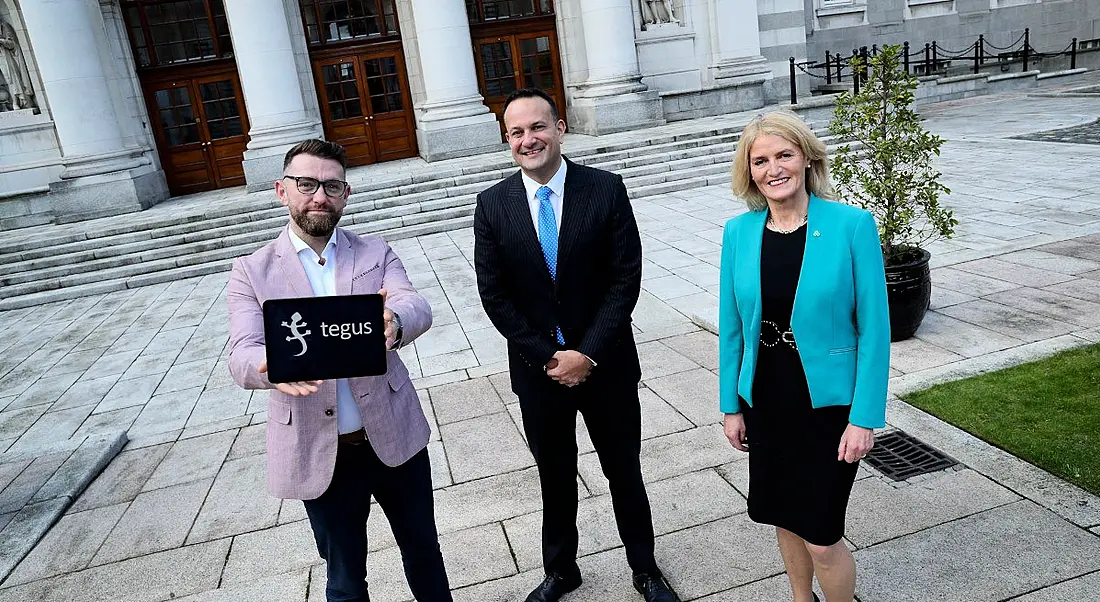 Three people stand outside Government buildings in Dublin, with one man holding a tablet that says 'Tegus' on the screen.