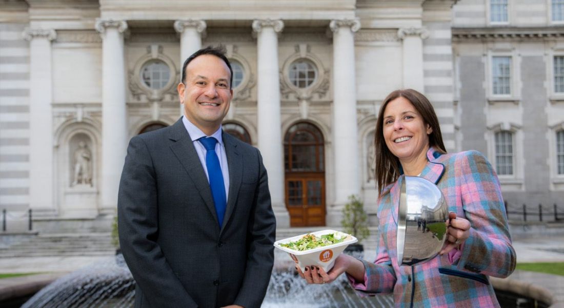 A woman outside Government buildings with the Tánaiste offers him a box filled with a takeaway salad.