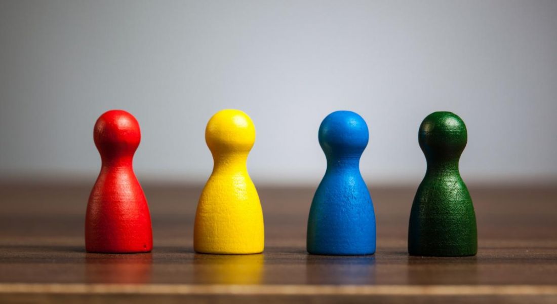 Four different coloured wooden figurines lined up on a table, representing neurodiversity.