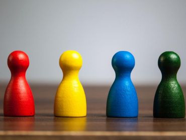 Four different coloured wooden figurines lined up on a table, representing neurodiversity.