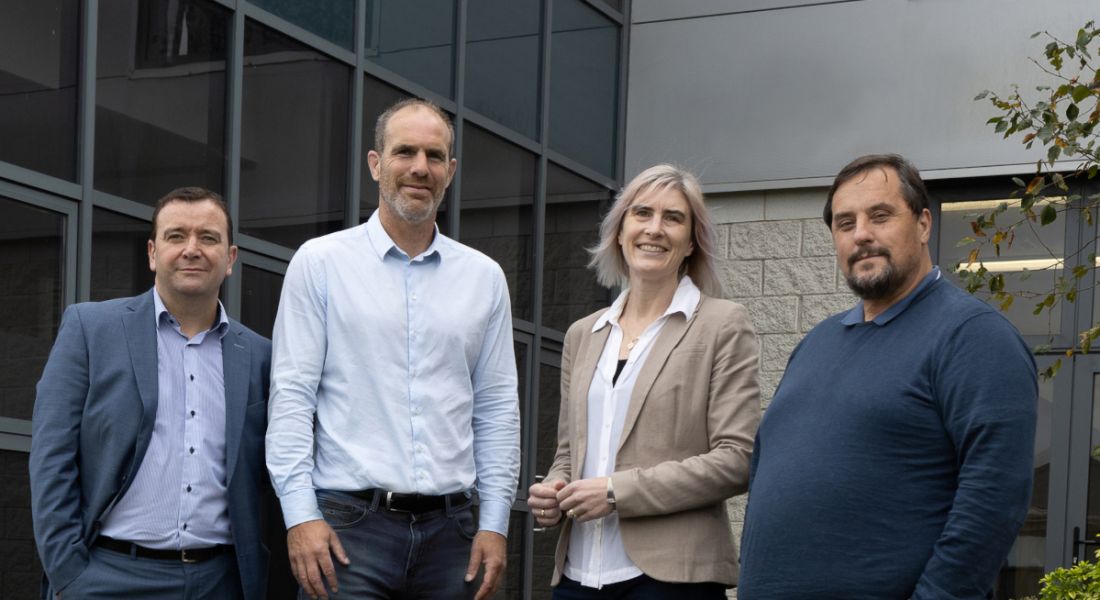 Cantec Group's Dara Madden, Greg Tuohy, Éadaoin Carrick, and Adrian Kelehan standing in a row and smiling at the camera in front of a grey brick and glass building.