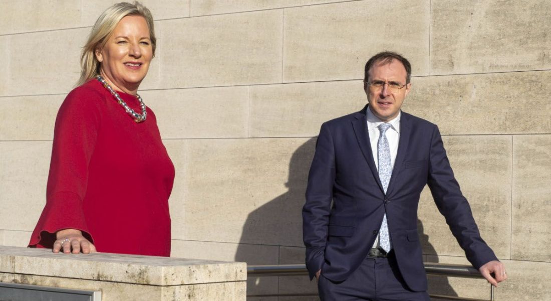 Carmel Owens and Robert Troy standing outside a building leaning on two different walls at a set of steps.