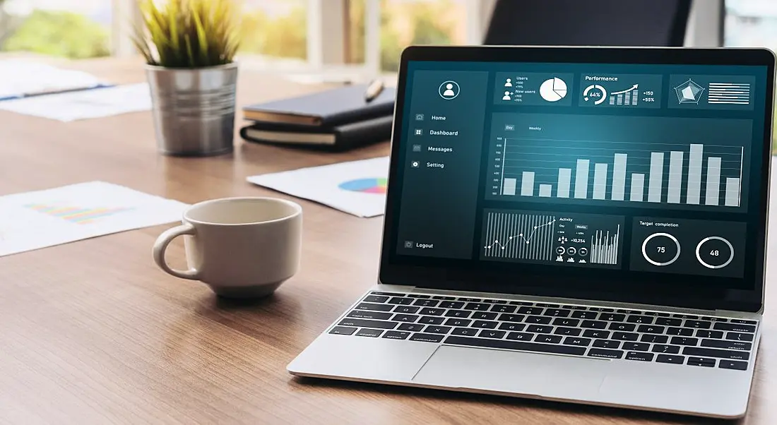 Laptop displaying data analytics platform on a table with a coffee cup beside it.