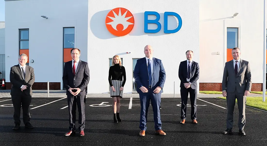 Six members of the BD team standing in front of a white BD building with company logo on the front.