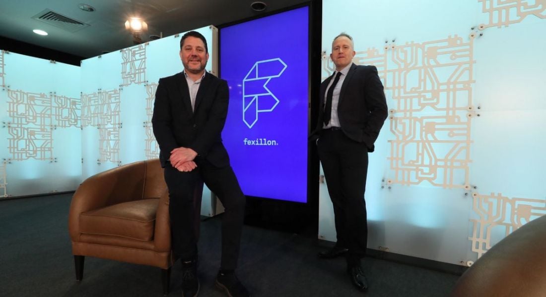 Kieran Beggan and George Harold with a Fexillon logo on a screen in the background and two brown armchairs near them.