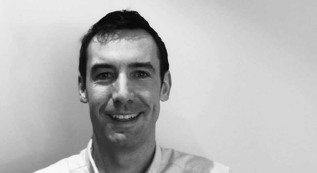 A black and white headshot of a man smiling at the camera.