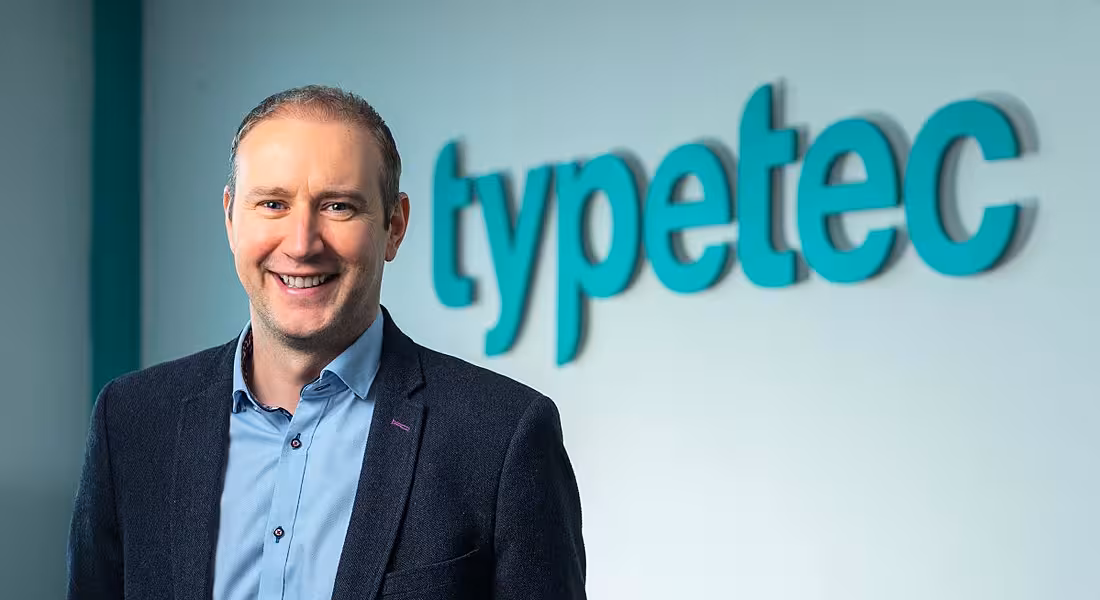 Headshot of Paul Dooley CEO of Typetec standing in front of a blue-lettered sign that reads Typetec.