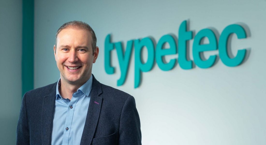 Headshot of Paul Dooley CEO of Typetec standing in front of a blue-lettered sign that reads Typetec.