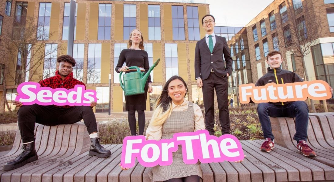 Three students sit outside a university with signs that say 'Seeds for the Future'. Behind them are a TU Dublin lecturer and Huawei Ireland's CEO.