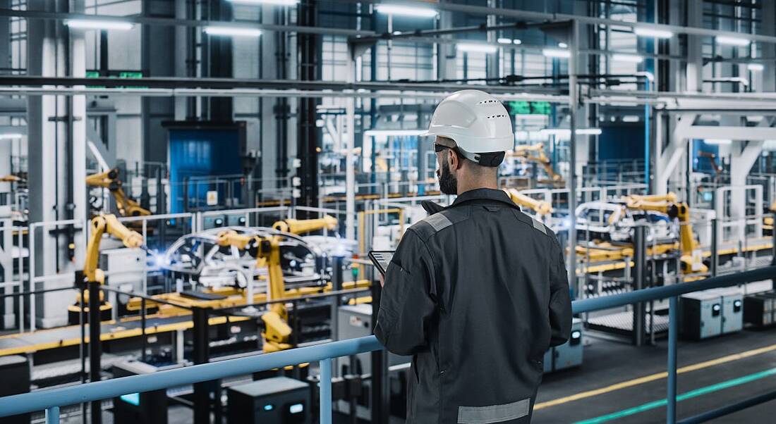 A man wearing a hard hat stands above a manufacturing floor, representing a deskless worker.