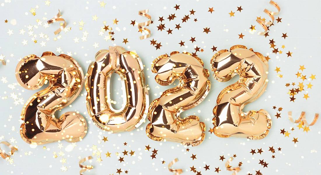 Gold foil balloons that spell out 2022 surrounded by gold star-shaped confetti on a light grey background.