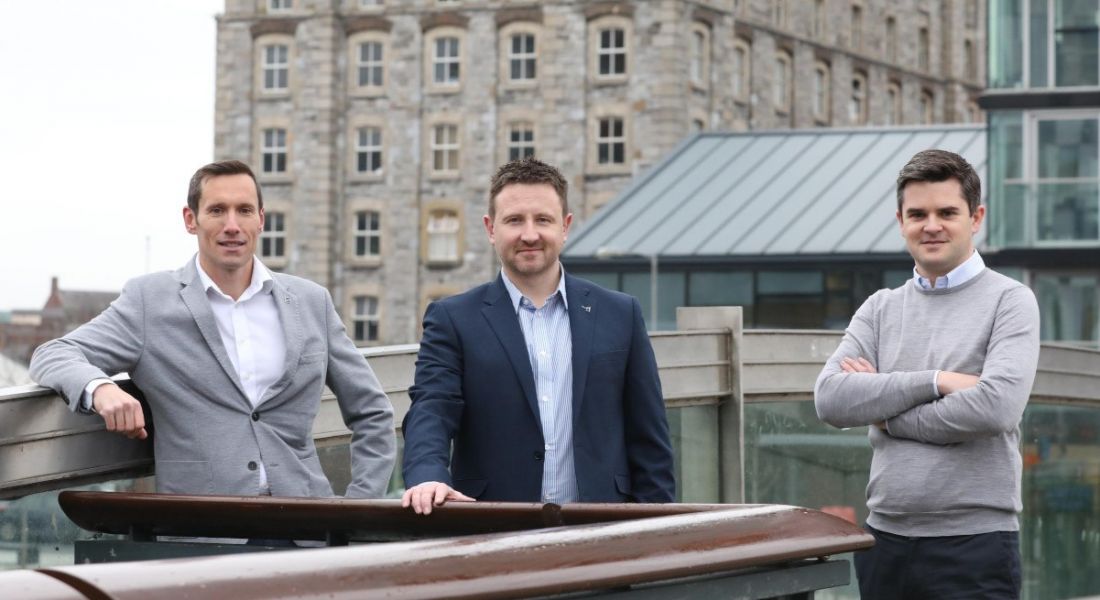 Three men stand on a rooftop in Waterford with buildings visible in the background.