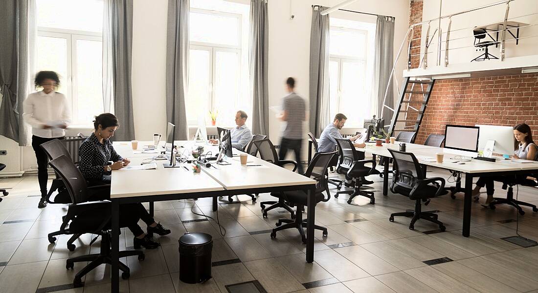 Modern office space featuring employees working at desks and walking around collaborating.