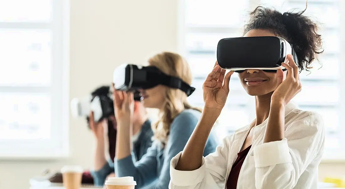 Row of students sitting at desks using virtual reality VR headsets in their lessons.