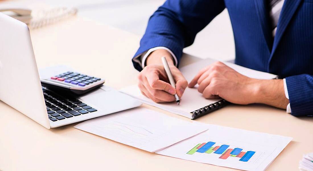 Business person working at a laptop analysing data and using a calculator.