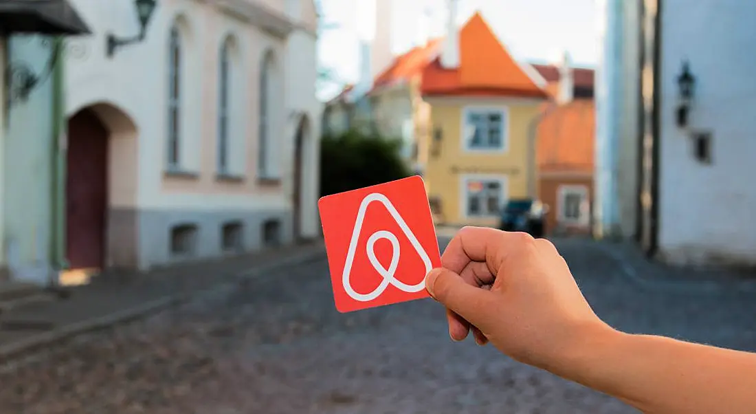 A person’s hand is holding up a card with the Airbnb logo on it against a cityscape of Minsk in Belarus.