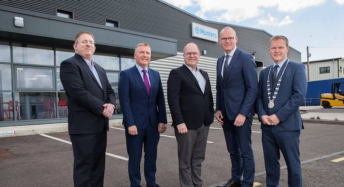 Five men in suits standing outside Munters manufacturing premises in Cork in a carpark on a cloudy day.