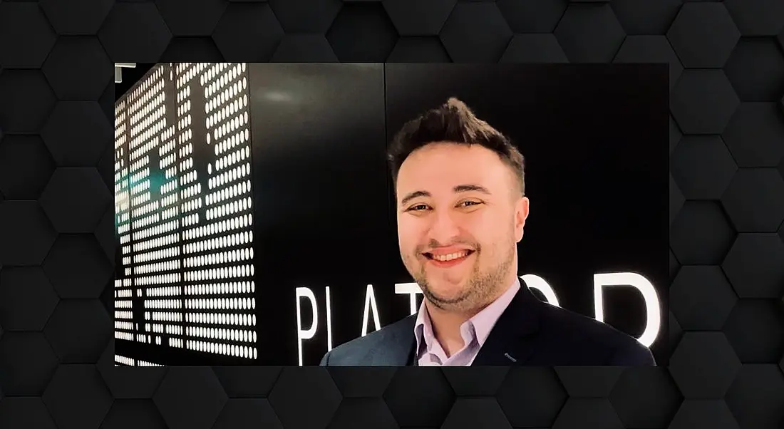 A man in a suit smiling at the camera in front of a large black wall with white lights on it.