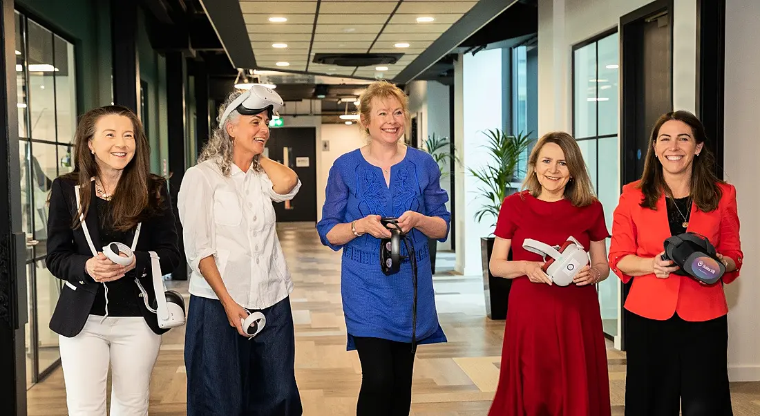 Five women pictured standing in a corridor holding VR headsets and immersive tech tools.