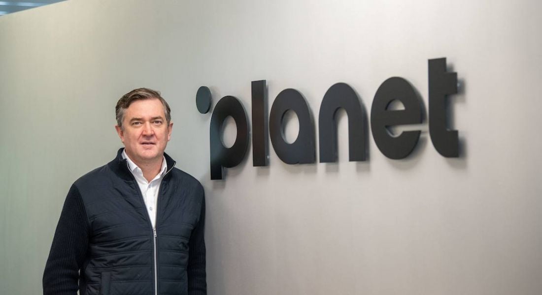 Man stands in front of a wall with a logo that reads ‘planet’.